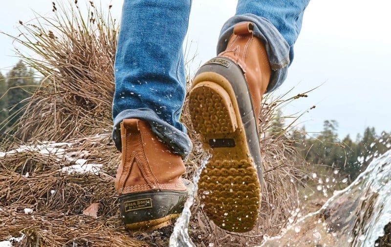 Boots stepping through water and grass on an outdoor trail. 