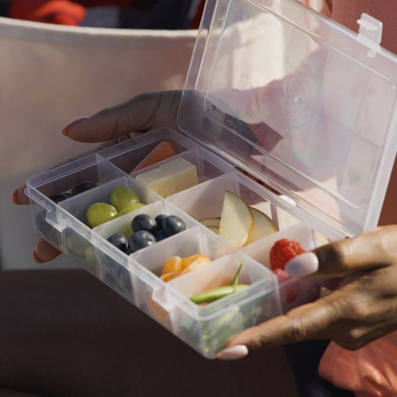A close-up of Stephanie holding an open pill organizer filled with different snacks.