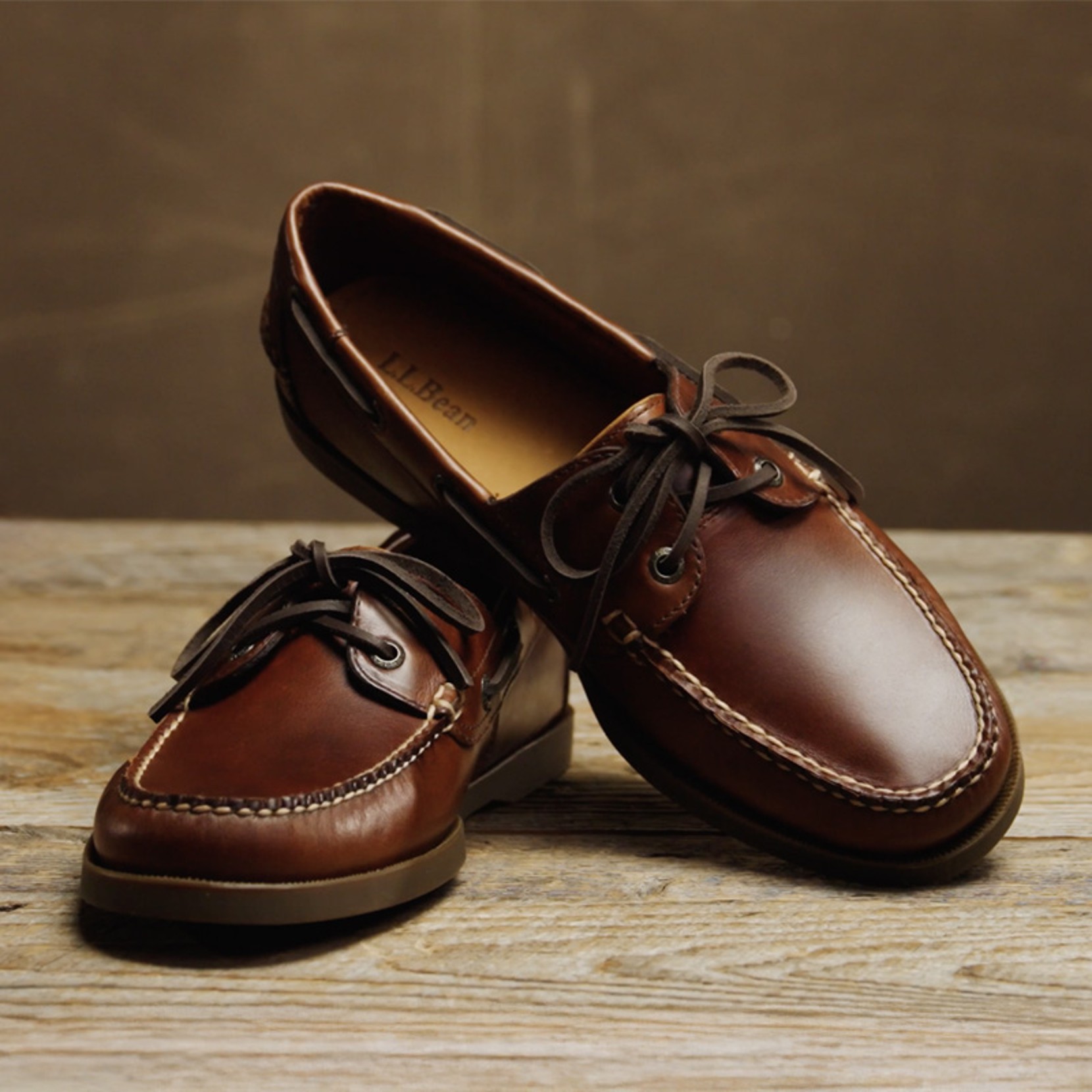 Pair of brown leather L L Bean boat shoes positioned on a rustic wooden tabletop.