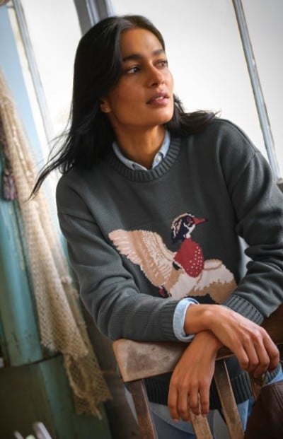 Person seated beside a window wearing a dark sweater with a duck design on the front.