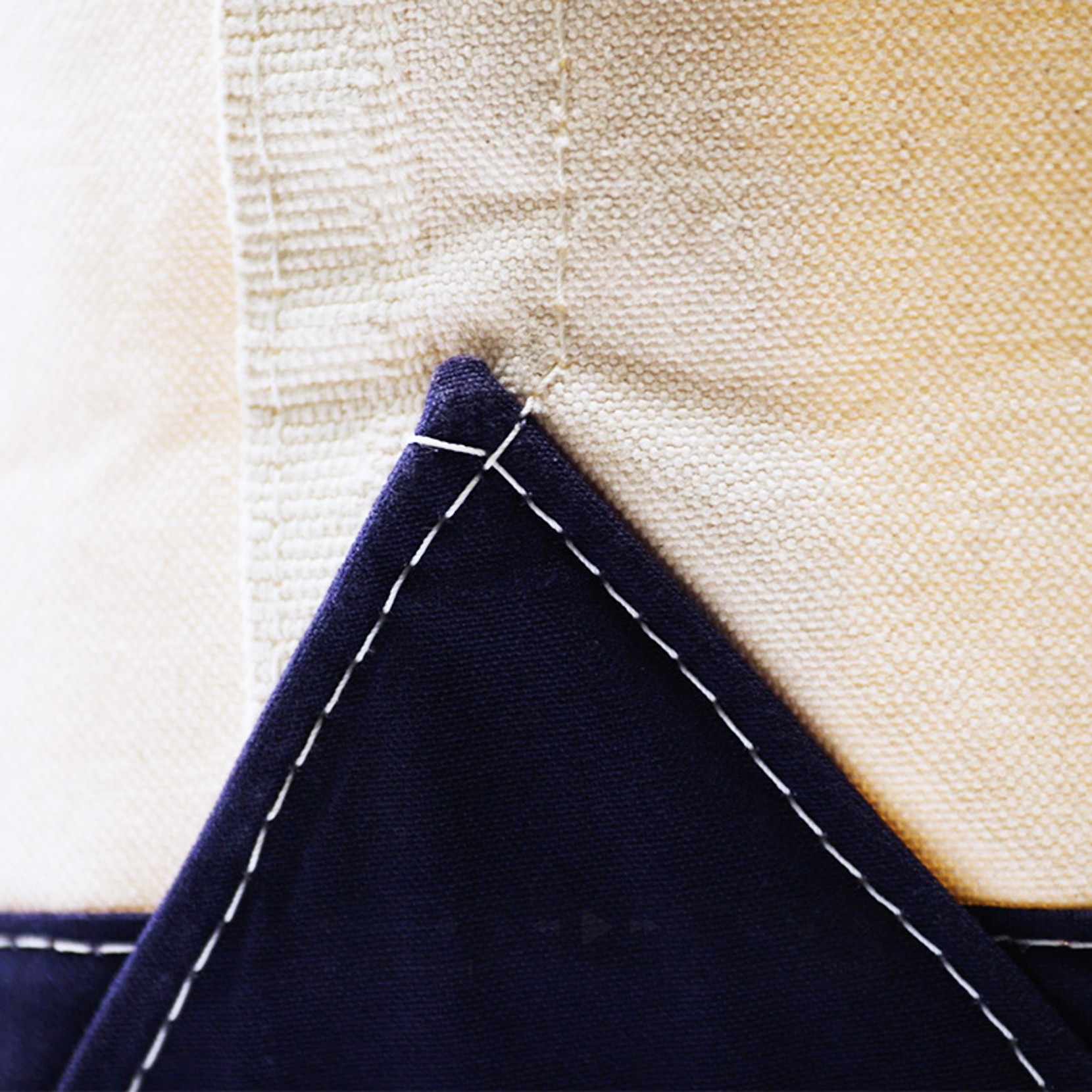 Close-up of beige and navy blue fabric with white stitching at the intersection of two cloth pieces.