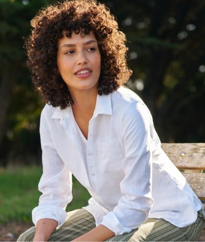 Woman outside on a bench, elbows resting on thighs.