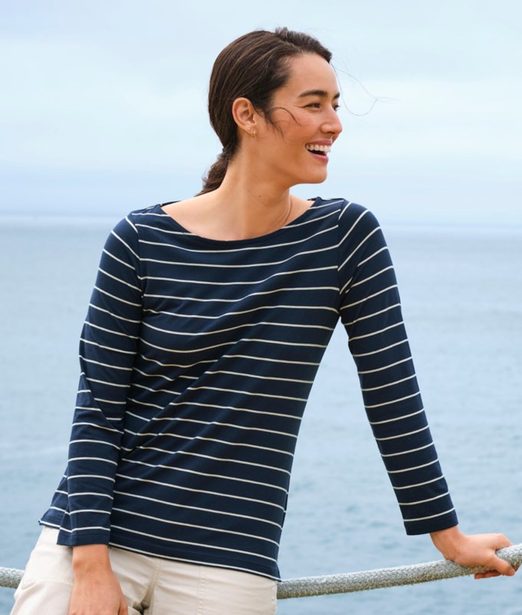 Brown haired woman in blue striped long sleeve tee shirt by water.