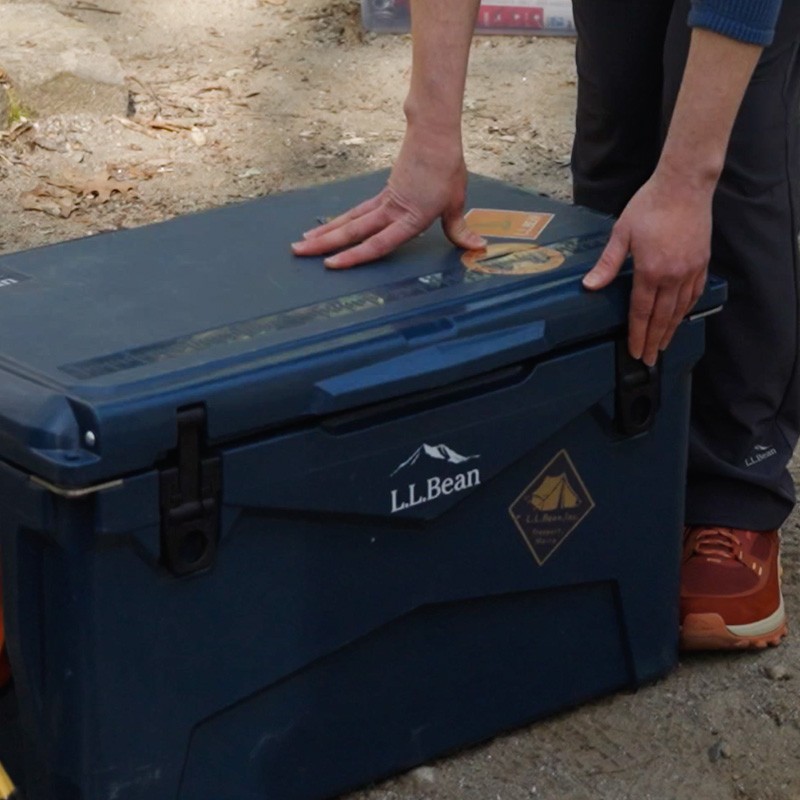 A person holding a blue L L Bean cooler by the lid, ready for an outdoor adventure.