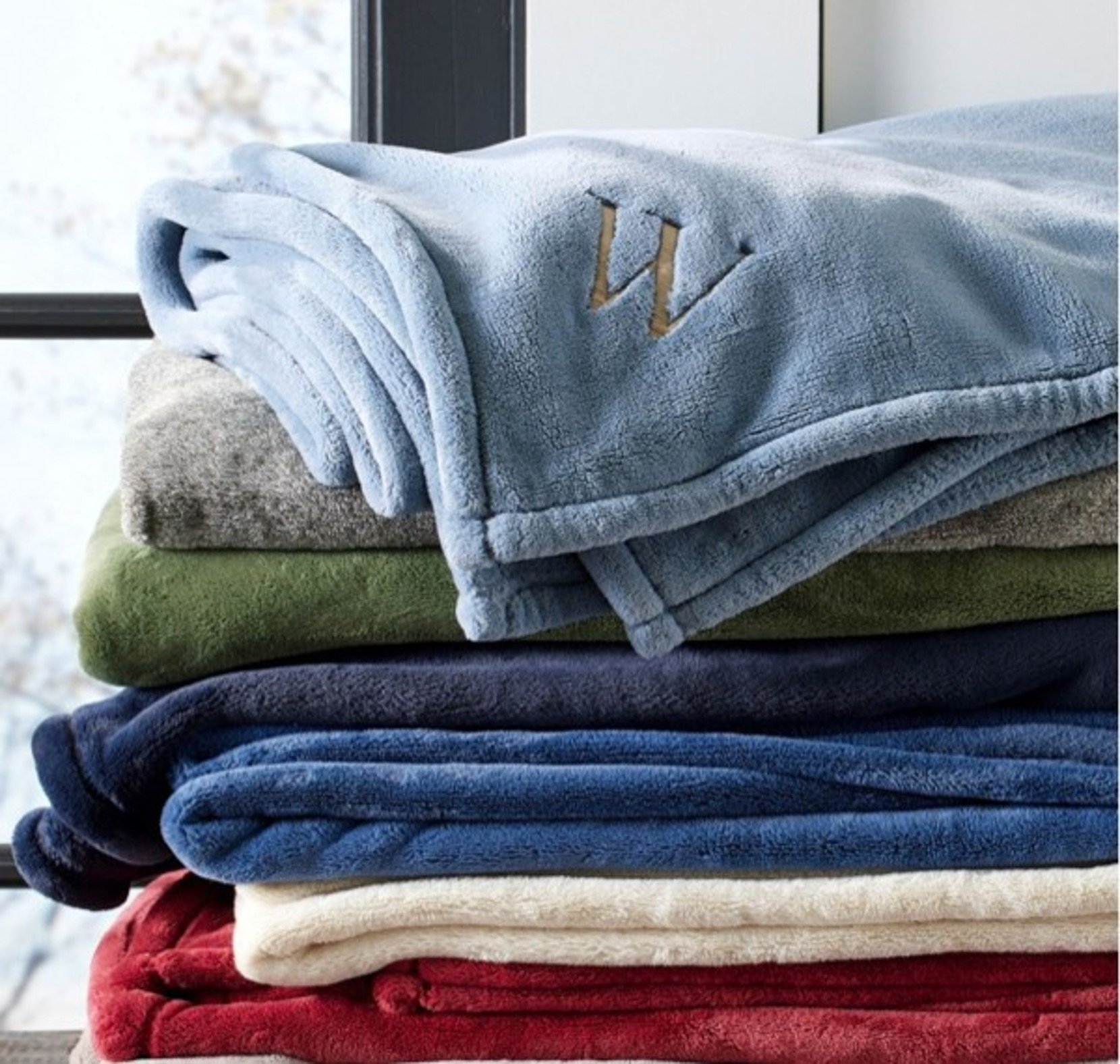 Monogrammed Fleece Throw draped over a colorful stack of fleece blankets