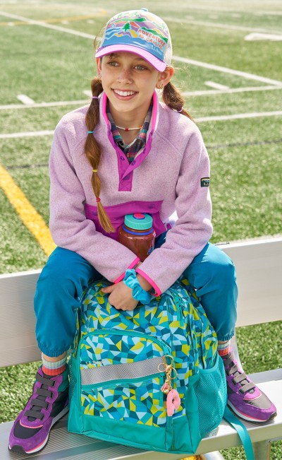A girl sitting on a bench at a football field with her Deluxe Book Pack.