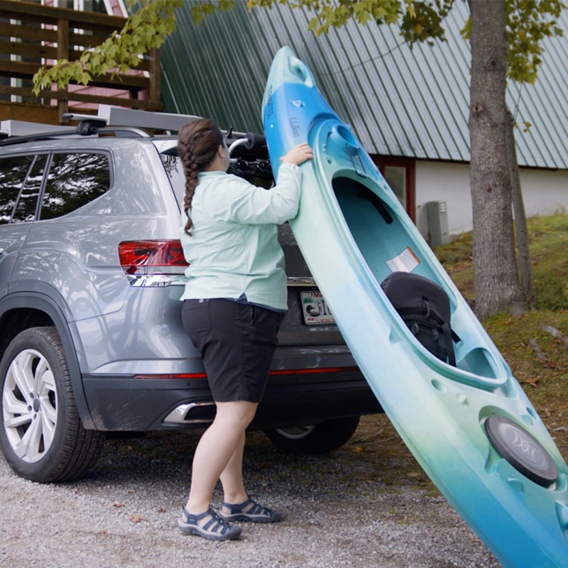 MacKenzie loading a kayak onto a car roof rack by herself.