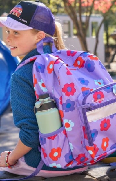 A child wearing a floral backpack with a water bottle attached to the side.
