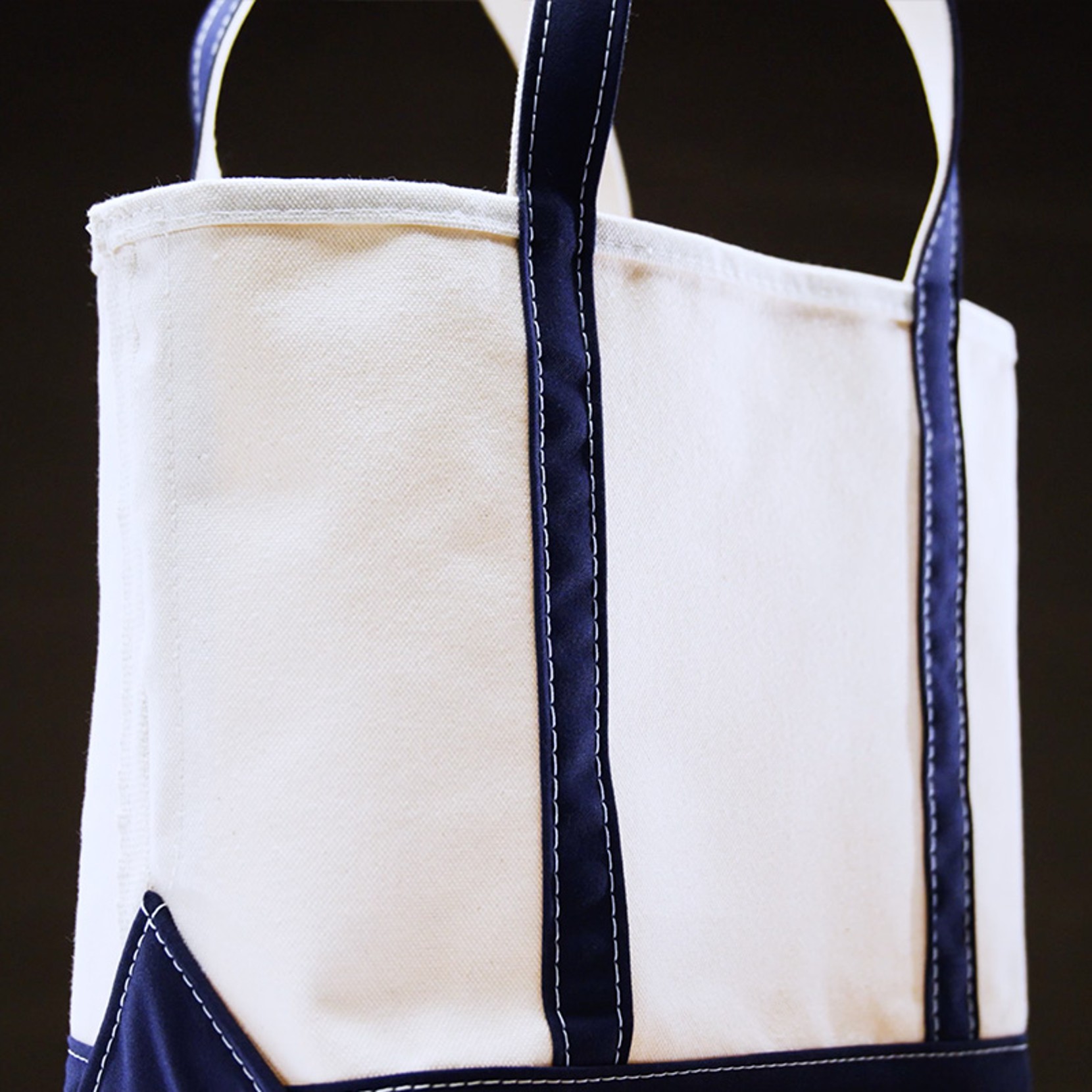 White canvas tote bag with dark blue handles and trim, featuring visible stitching details.