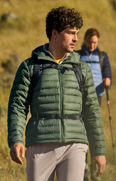 Person walking outdoors in a green puffer jacket with another person in the background.
