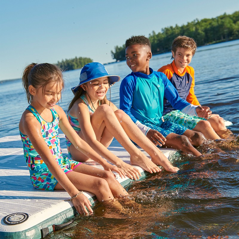 4 kids sitting on a dock, feet in the water.