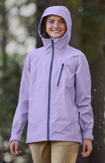 Person wears a light purple hooded rain jacket and tan pants while standing outdoors in light rain.