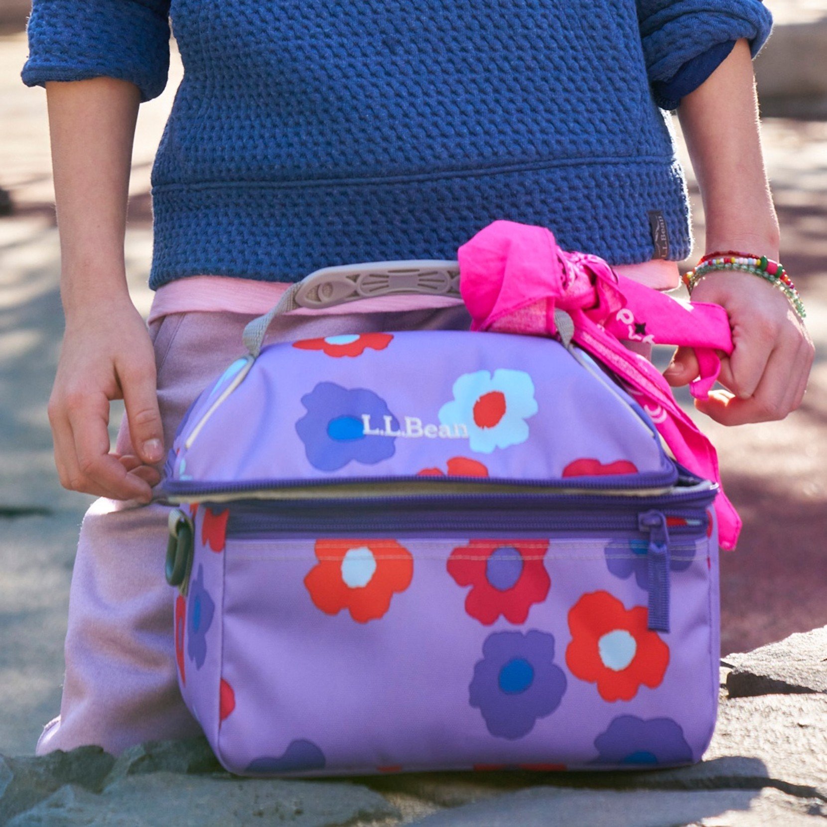 A purple flower motif lunch box on a rock wall with a young person standing behind it.