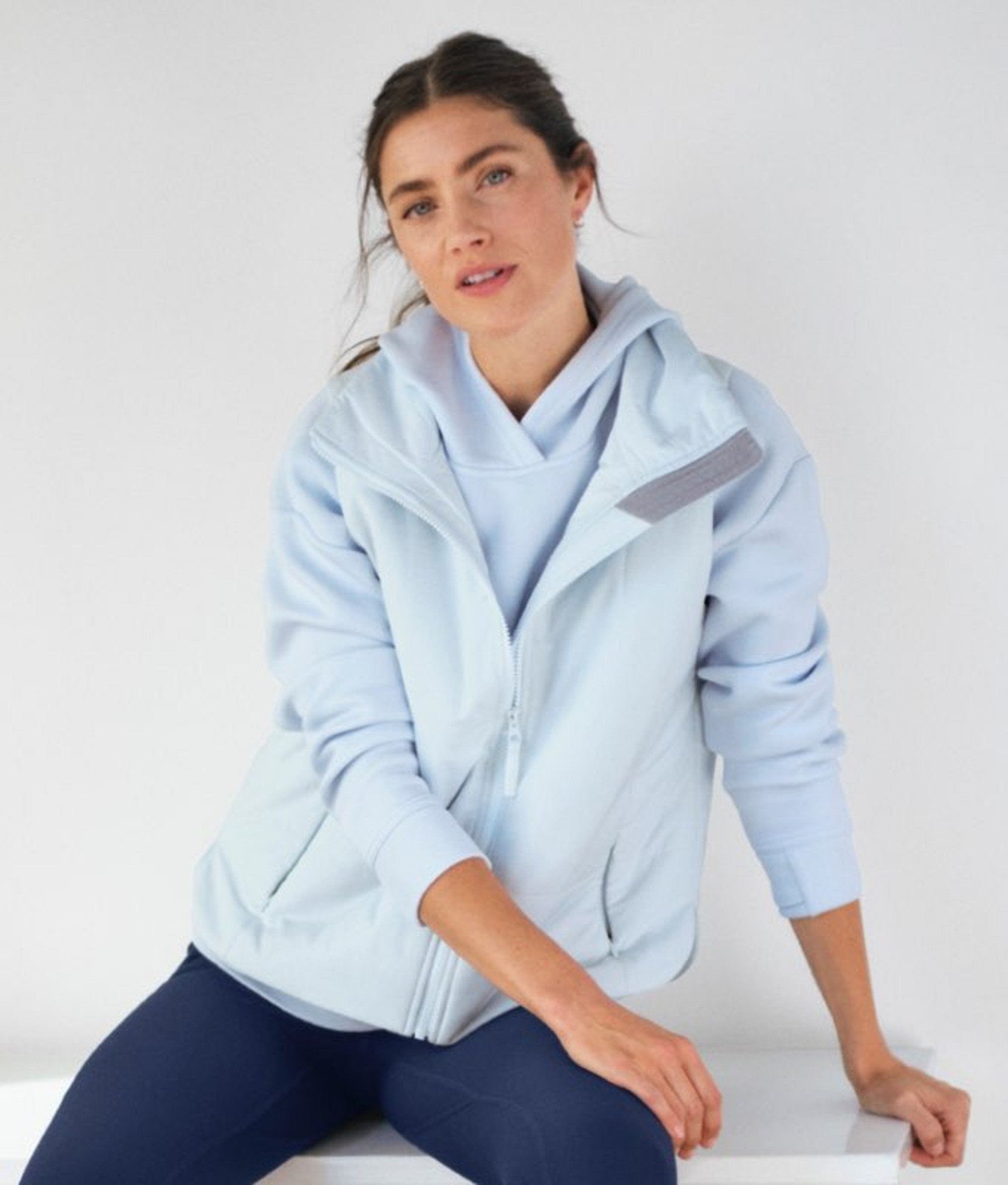 Light blue women’s activewear hoodie worn by a seated model. 
