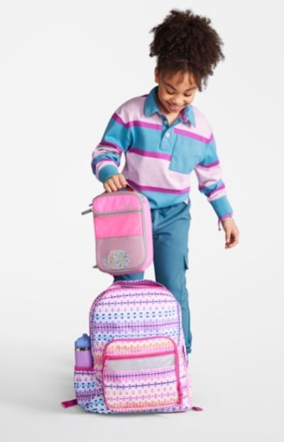 A young girl on the floor looking at her school backpack and accessories.