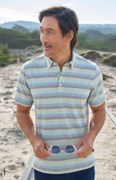 Waist up shot of a man outside wearing a blue striped polo shirt