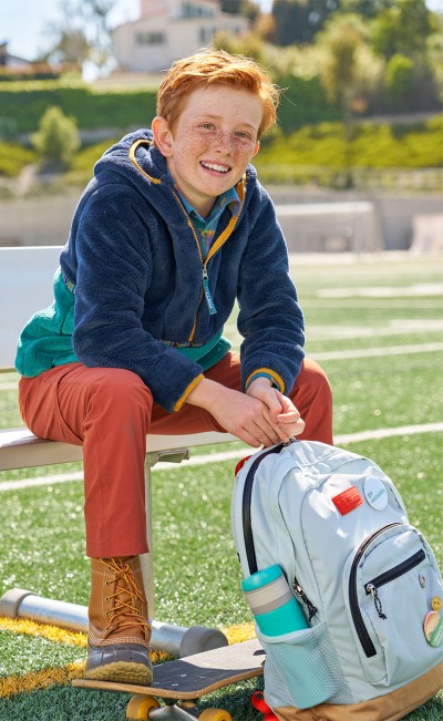 A boy sitting on a football field with his Mountain Classic School Backpack.
