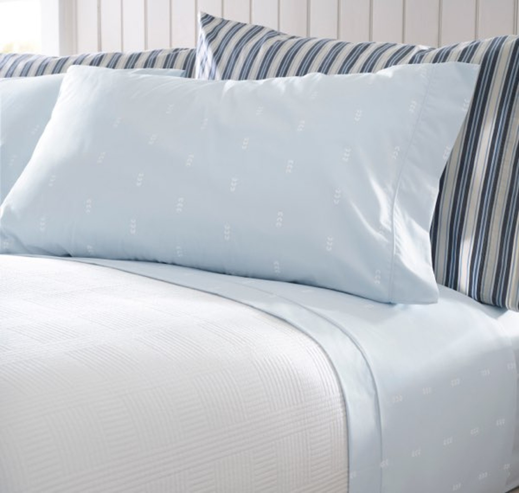 Light blue percale bed sheets neatly folded on a made bed. 