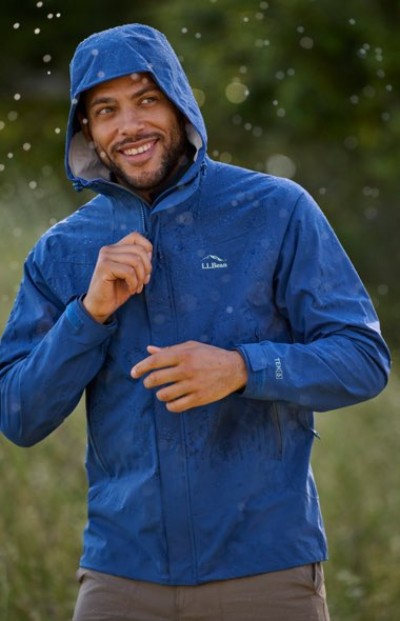 Person zipping up a blue hooded rain jacket while standing outside on a wet day.