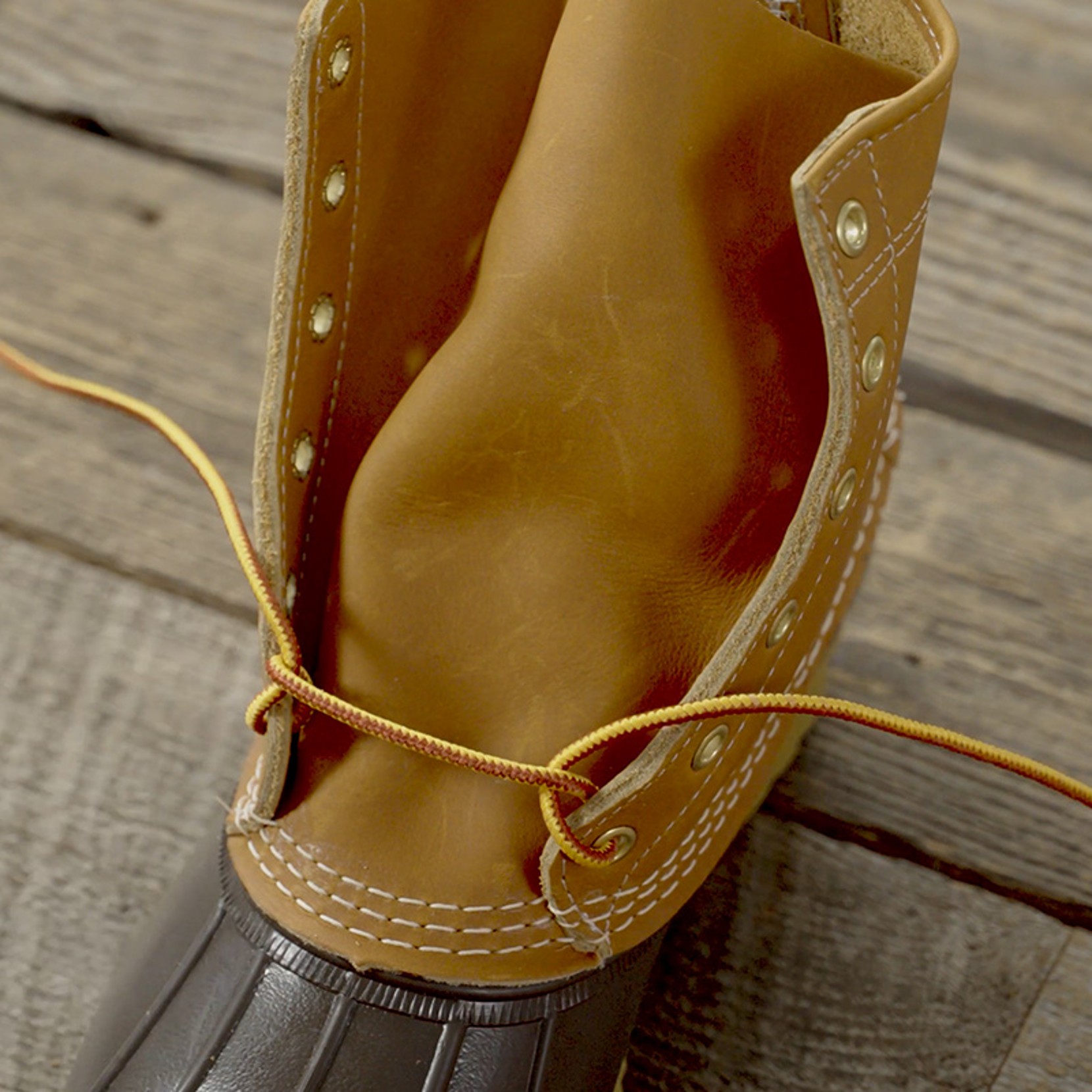 Close-up of open tan leather boot with yellow laces on a wooden surface.