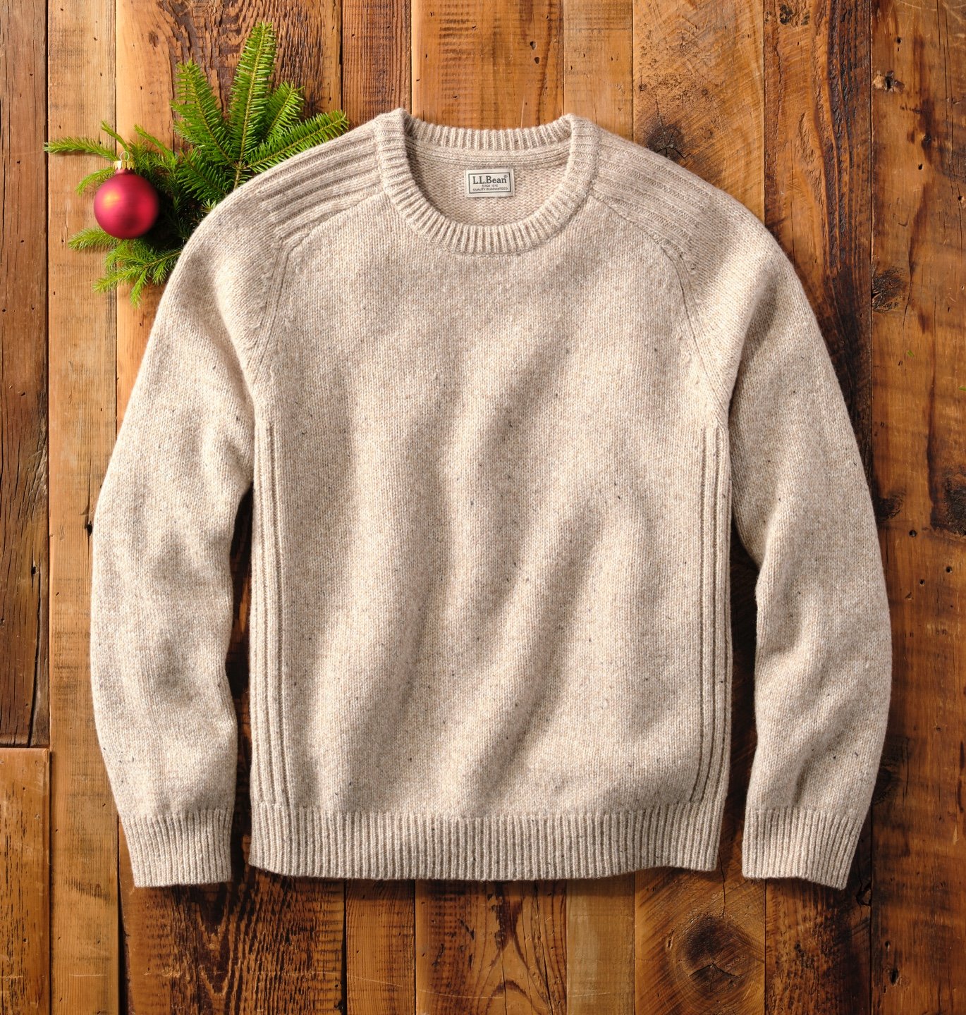 Light colored sweater laid out on a wooden floor with a pine branch.