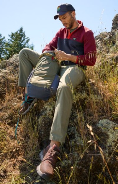 Person seated on a grassy slope wearing outdoor apparel and a baseball cap.