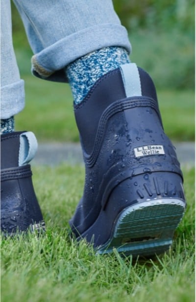 Close-up of a person in dark blue rain boots and blue socks walking on grass.
