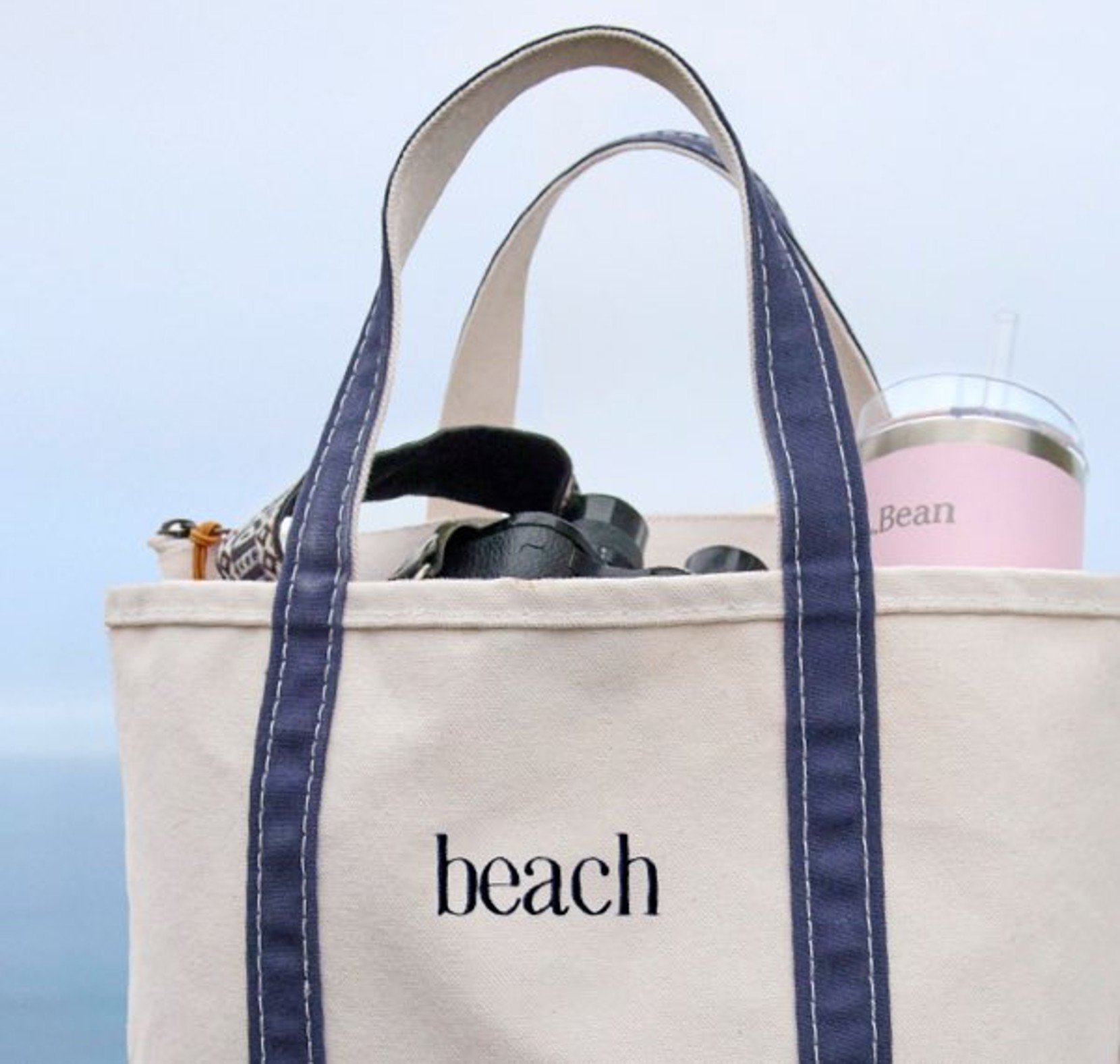 Canvas beach tote bag with navy straps and beach essentials peeking out at the top.
