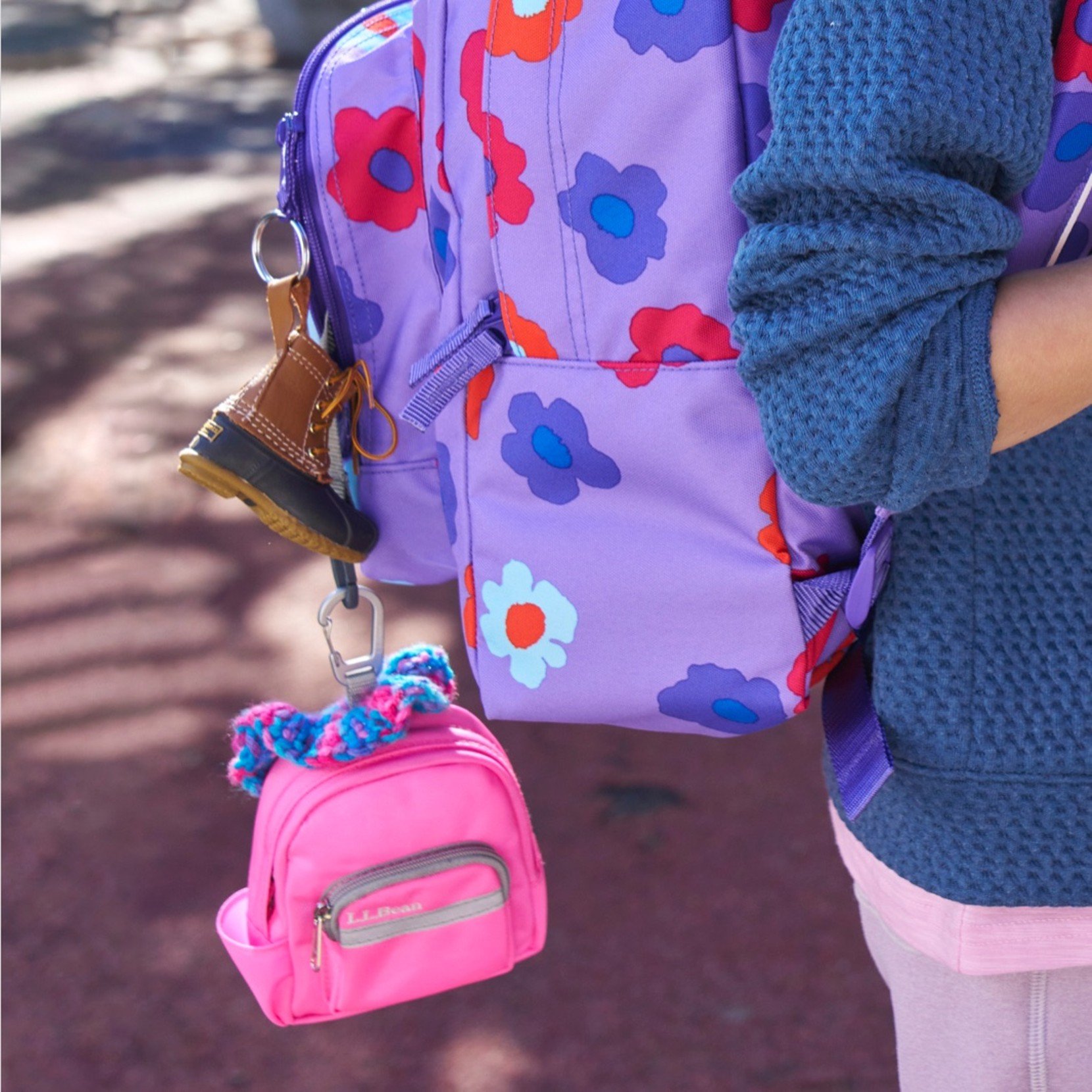 Close-up of a purple flower motif school backpack on the back of a young person with accessories hanging from it.