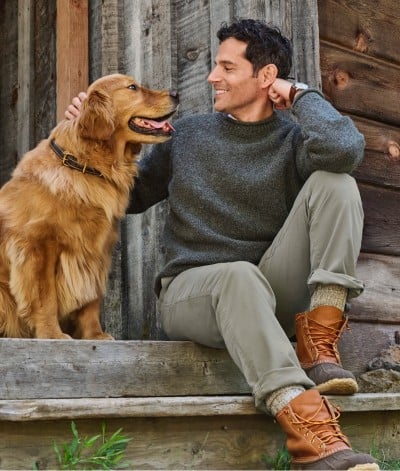 Man sits on cabin steps, petting a happy golden retriever.