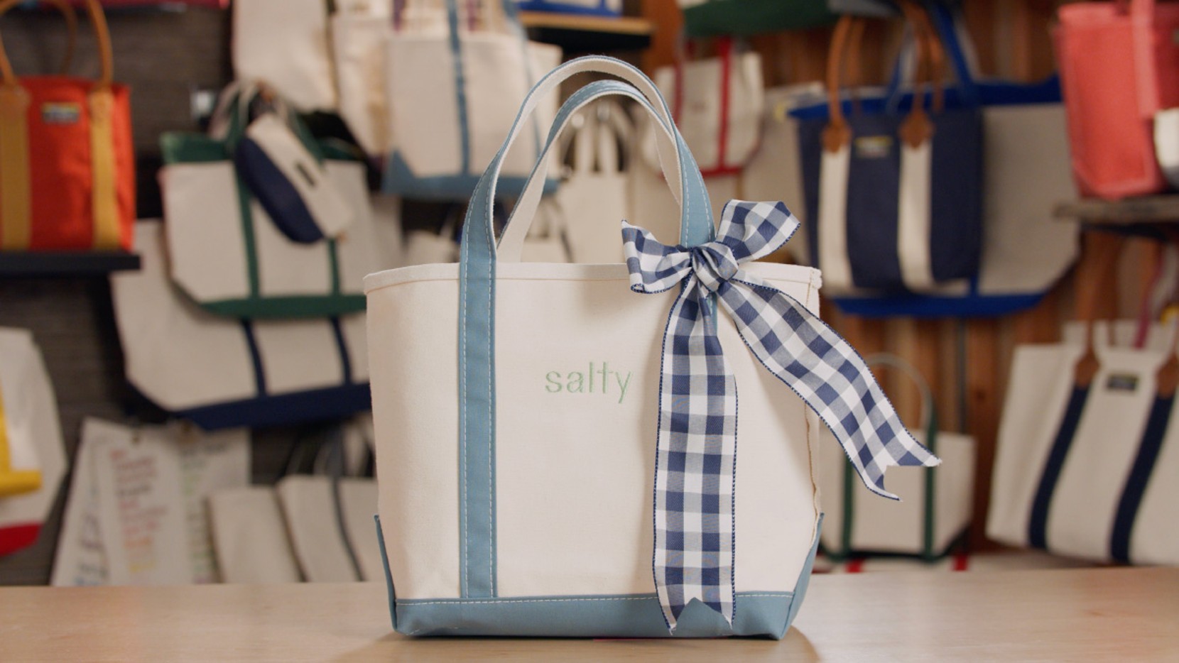 A Boat & Tote with light blue handles and a light blue monogram - salty, a navy gingham bow tied on the handle.