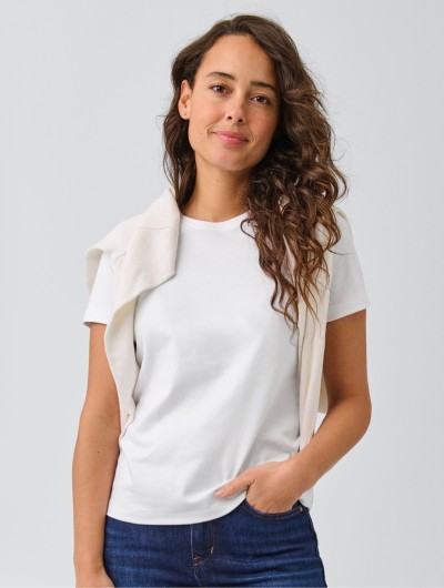 A thigh-up image of a woman wearing jeans and a white t-shirt, sweater draped across shoulders.