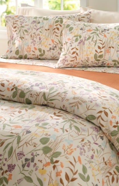 A neatly folded bed with an earth tone floral printed bedding.