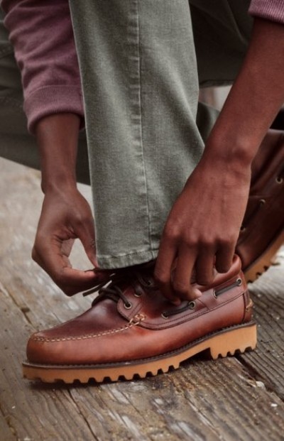 Close up of hands tying brown leather shoes while seated on a wooden deck.