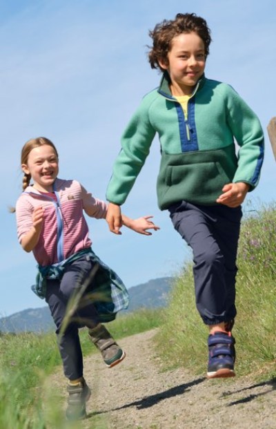 Two children running hand in hand along a grassy path near the water.