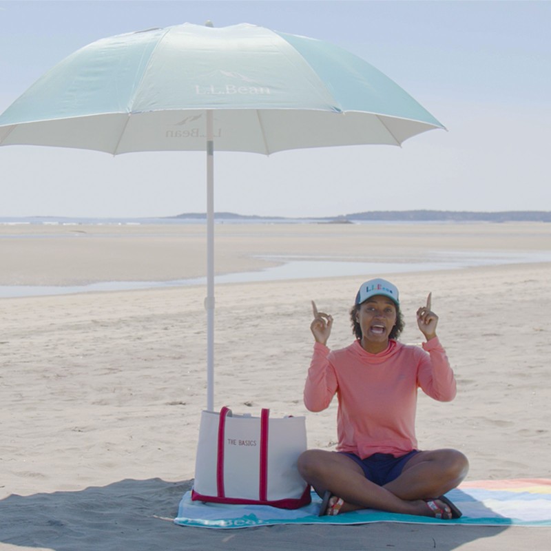 Stephanie sitting on a towel on the beach under an umbrella.