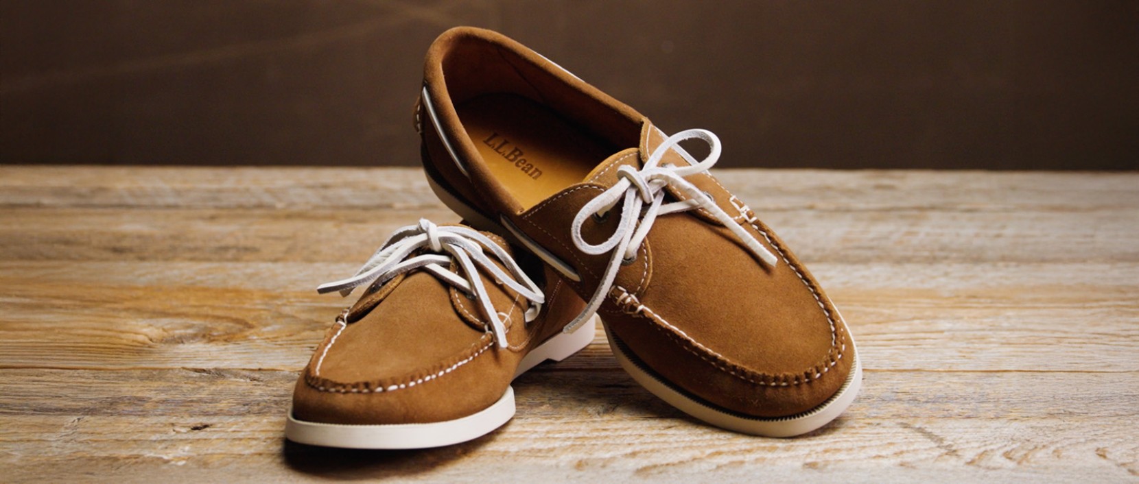 Brown suede L L boat shoes with white laces displayed side by side on a wooden surface.