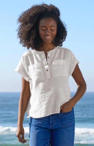 Person wearing a white short‑sleeve top and jeans standing outdoors by the ocean.