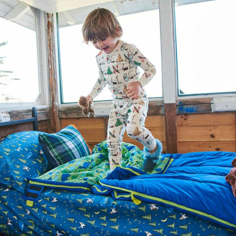 A happy kid standing on a sleeping bag covered twin bed in a screened in cabin.