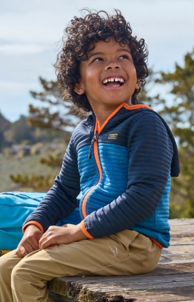 A young child sitting on a rock wearing a blue colorblock hoodie and tan pants.