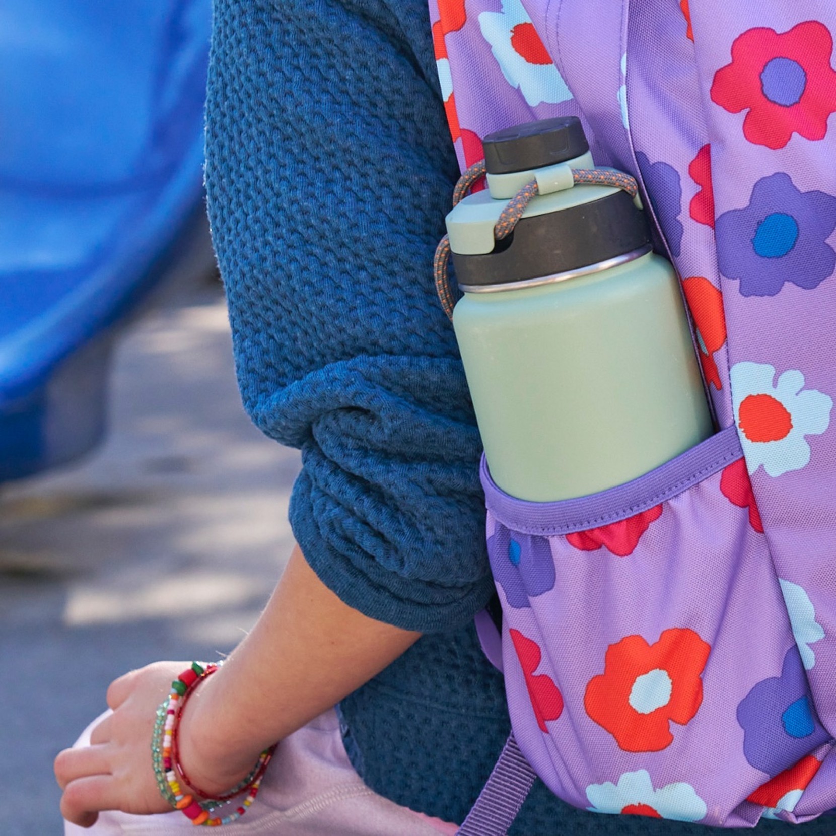Close-up of a purple flower motif school backpack on the back of a young person with a water bottle in the side pocket.
