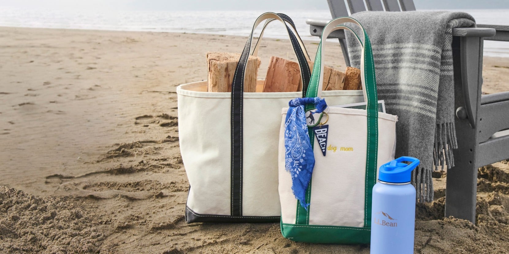 Canvas tote bags with firewood beside a beach chair, blanket, and water bottle on a sandy beach.