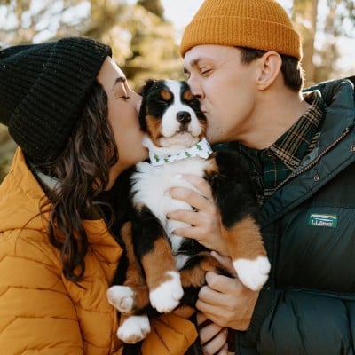 A couple holding a puppy between them, each kissing the puppy's head.