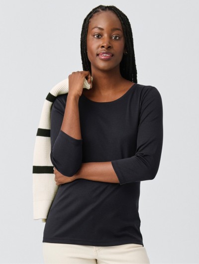 A thigh-up shot of a woman wearing a black long-sleeve t-shirt holding a black and white striped sweater across one shoulder.
