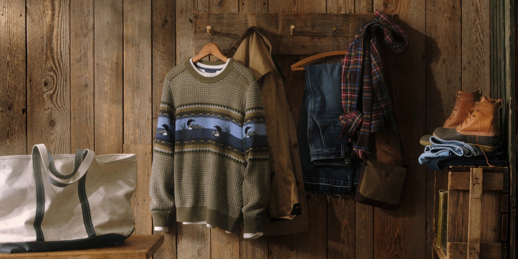 Rustic display of fall clothing, duck boots and tote bag hanging against a wooden wall.
