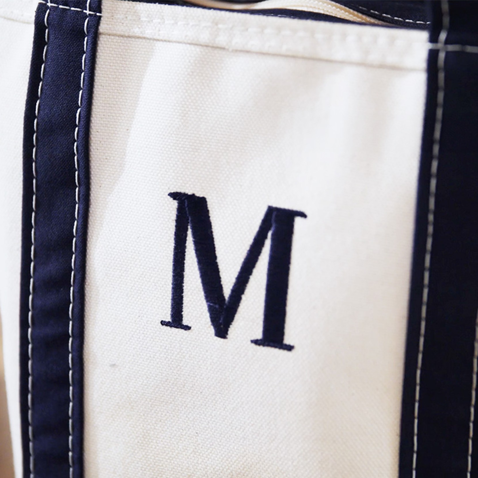 Close-up of white canvas bag with navy trim and embroidered navy letter “M” on the front.