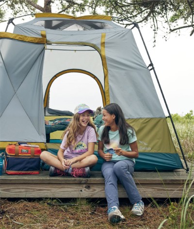 Two girls sitting outside the front of their tent while camping.