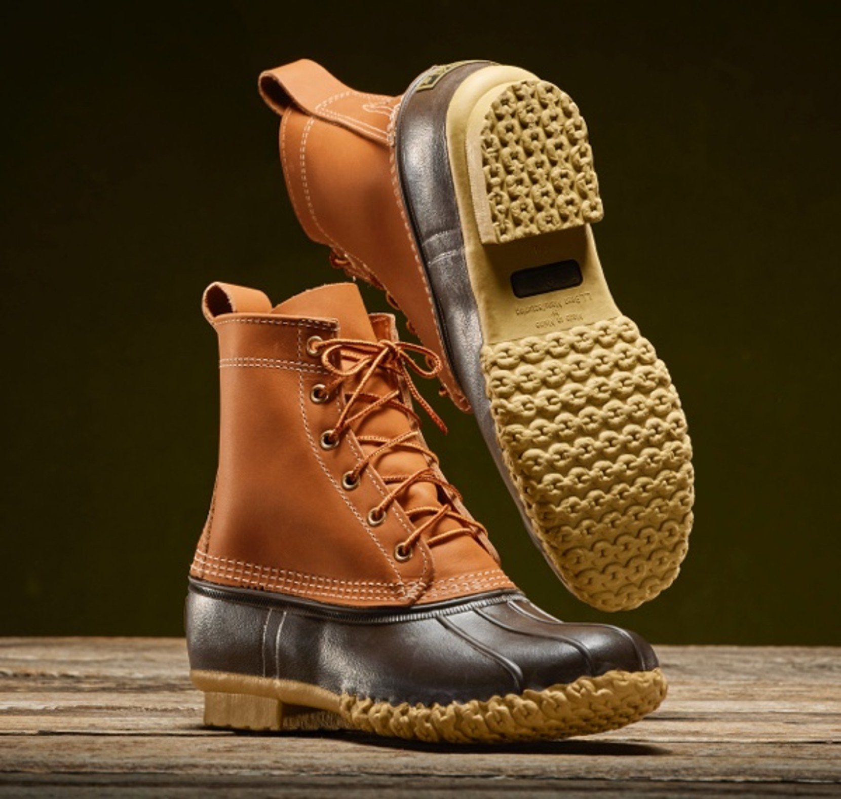 Brown leather duck boots with rubber soles displayed on a rustic wooden surface.