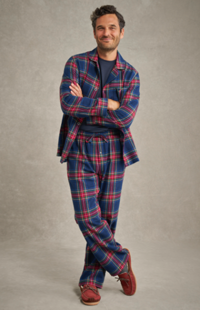 A man wearing blue and red plaid flannel pajamas stands with arms crossed, wearing brown slippers.