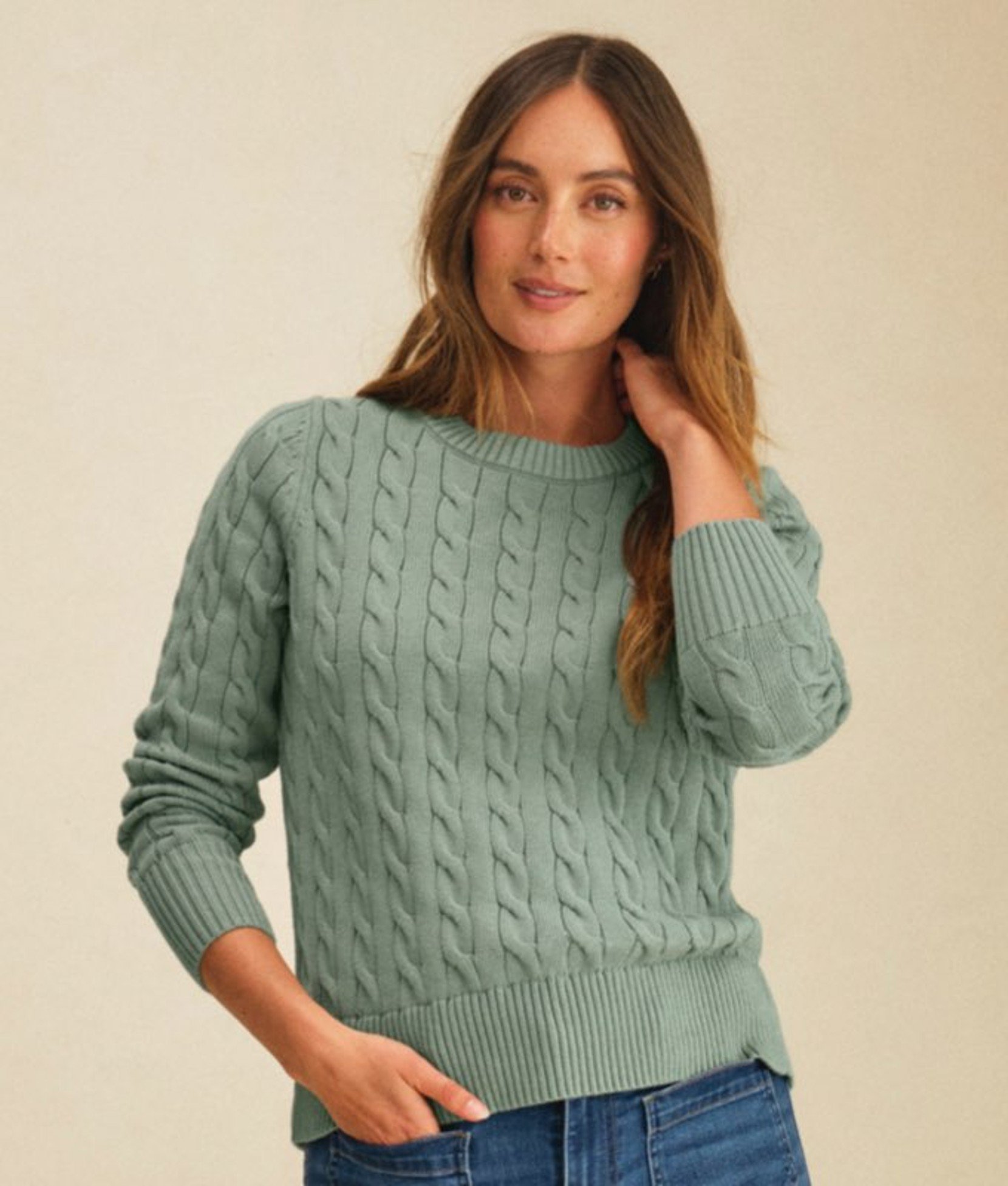 Person wearing a green cable-knit sweater with hands in pockets.